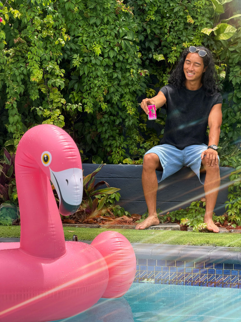A man sitting by a pool with an inflatable flamingo floaty, holding a Lick Energy drink.