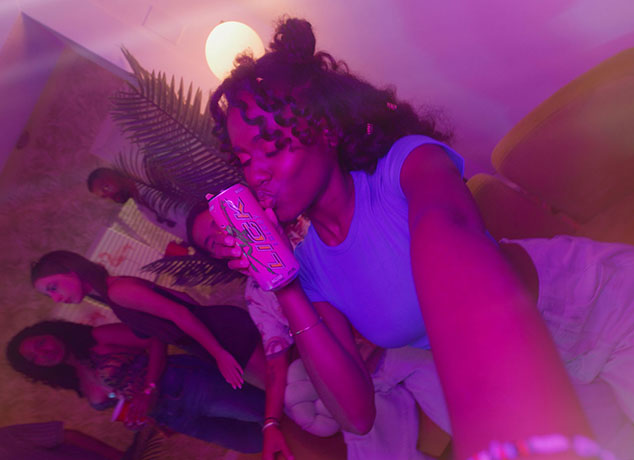 Group of people in a room with purple lighting, one person holding a Lick Energy.