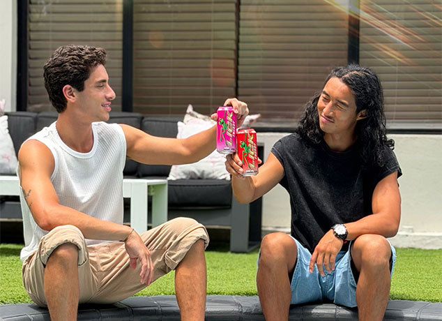 Two men sitting outdoors, holding Lick Energy drinks.