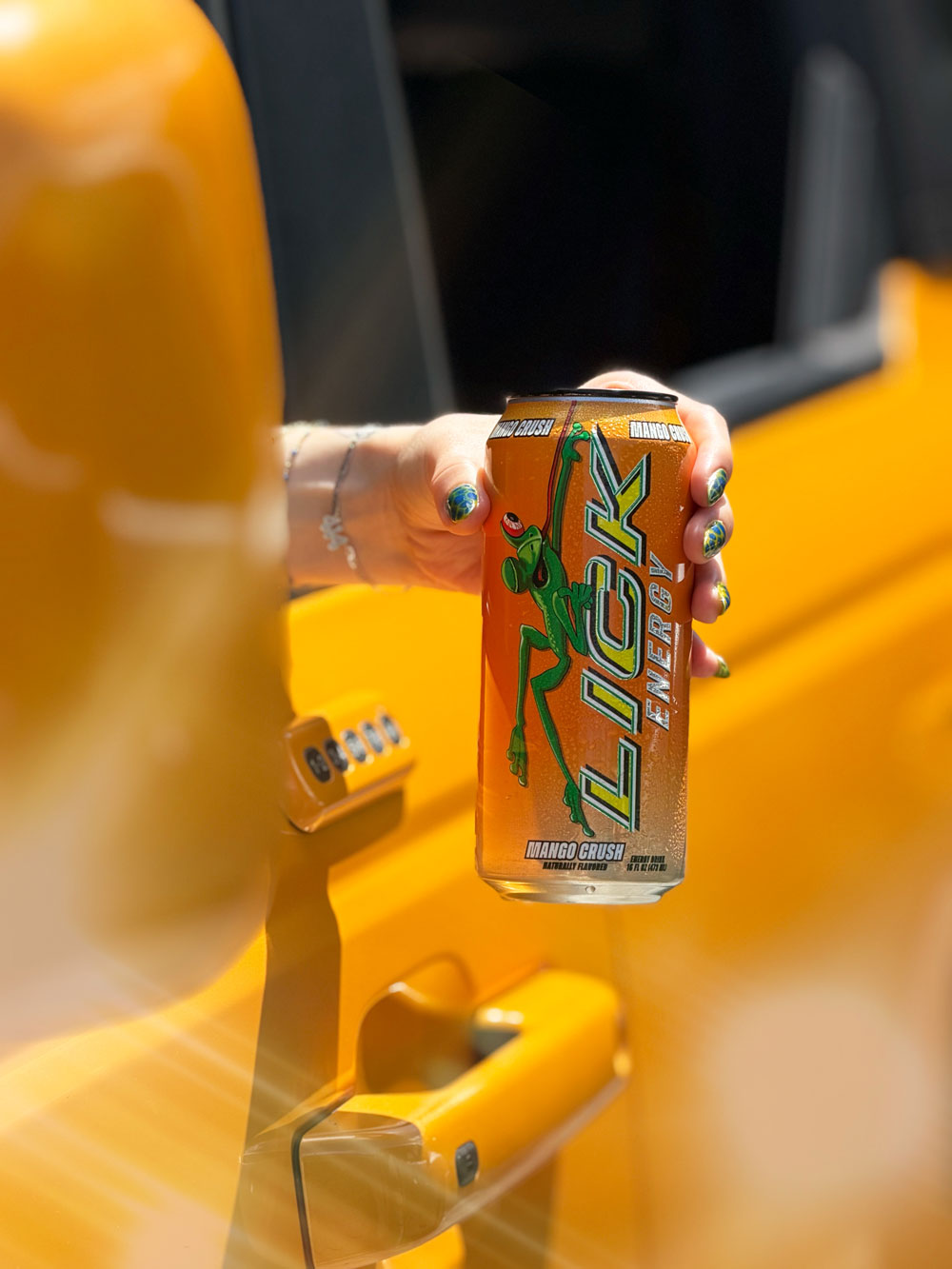 Person holding a Lick Energy drink can with a yellow vehicle in the background