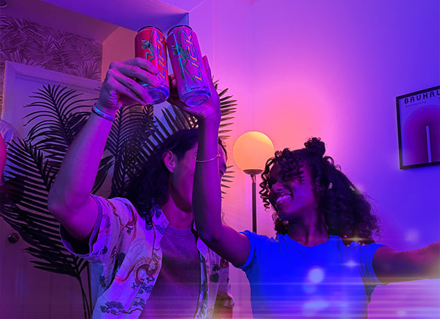 Two people holding Lick Energy cans in a room with purple lighting