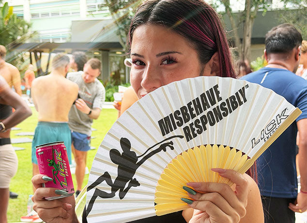 A woman holding a fan and a can of Razzade Lick Energy drink outdoors.