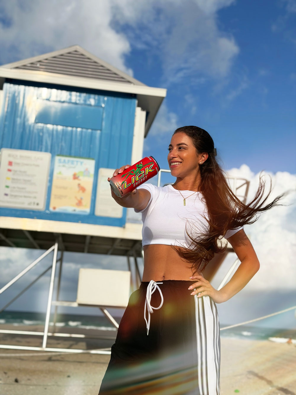 Woman holding LICK Energy in front of a lifeguard station on a beach