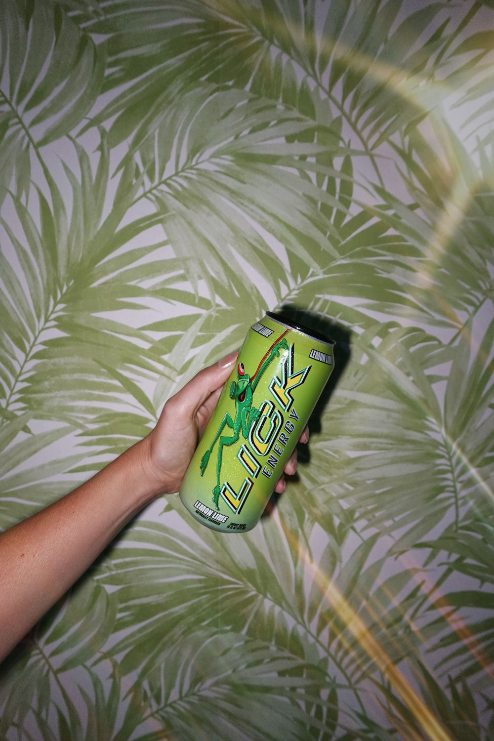 Hand holding a green can of Lick Energy against a leafy green background