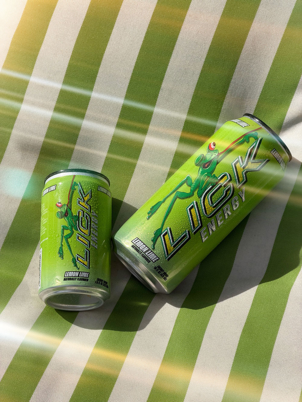 Two green LICK Energy drink cans on a striped green and white surface