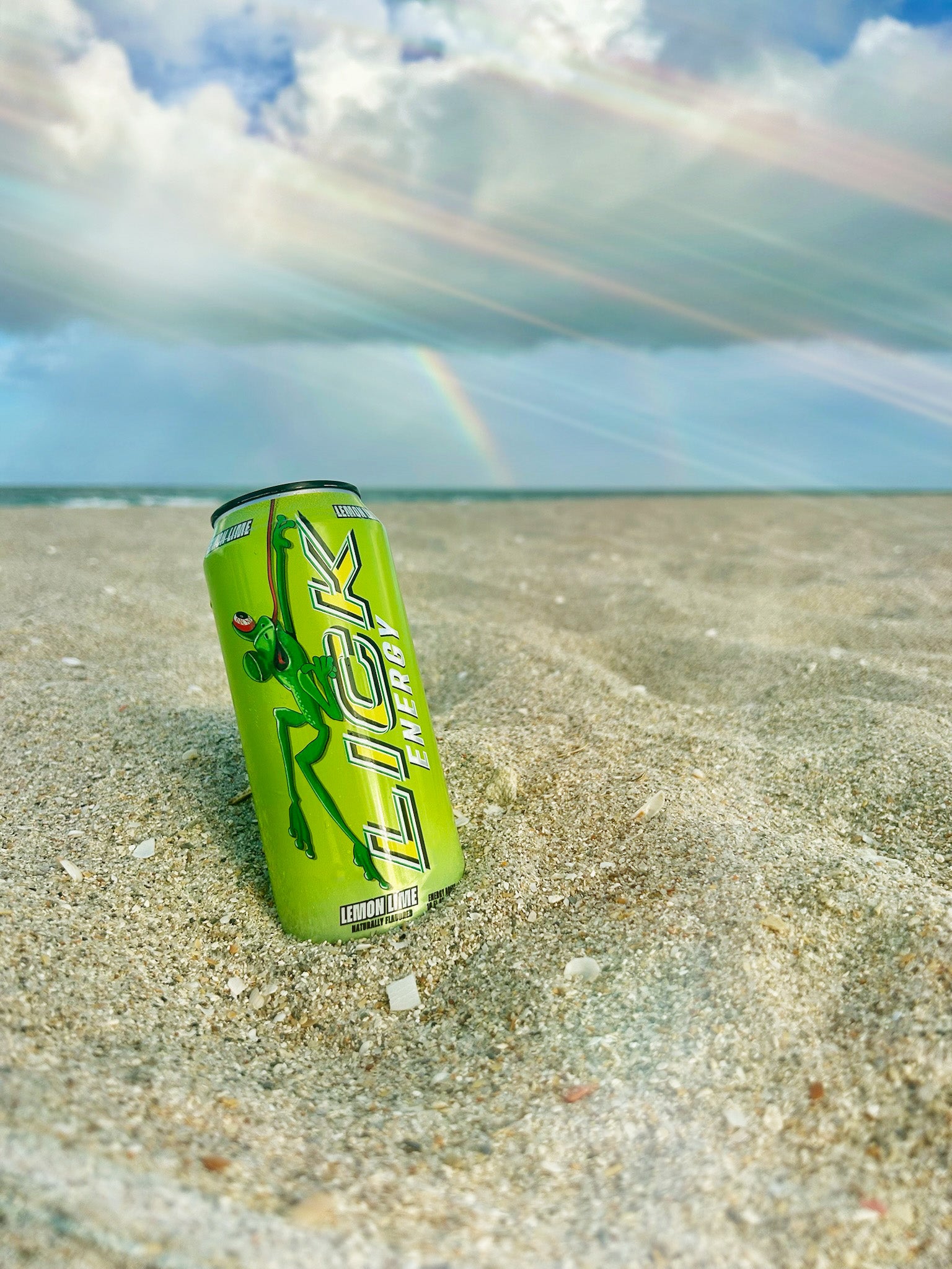 Lick energy drink can on a beach with a rainbow in the background