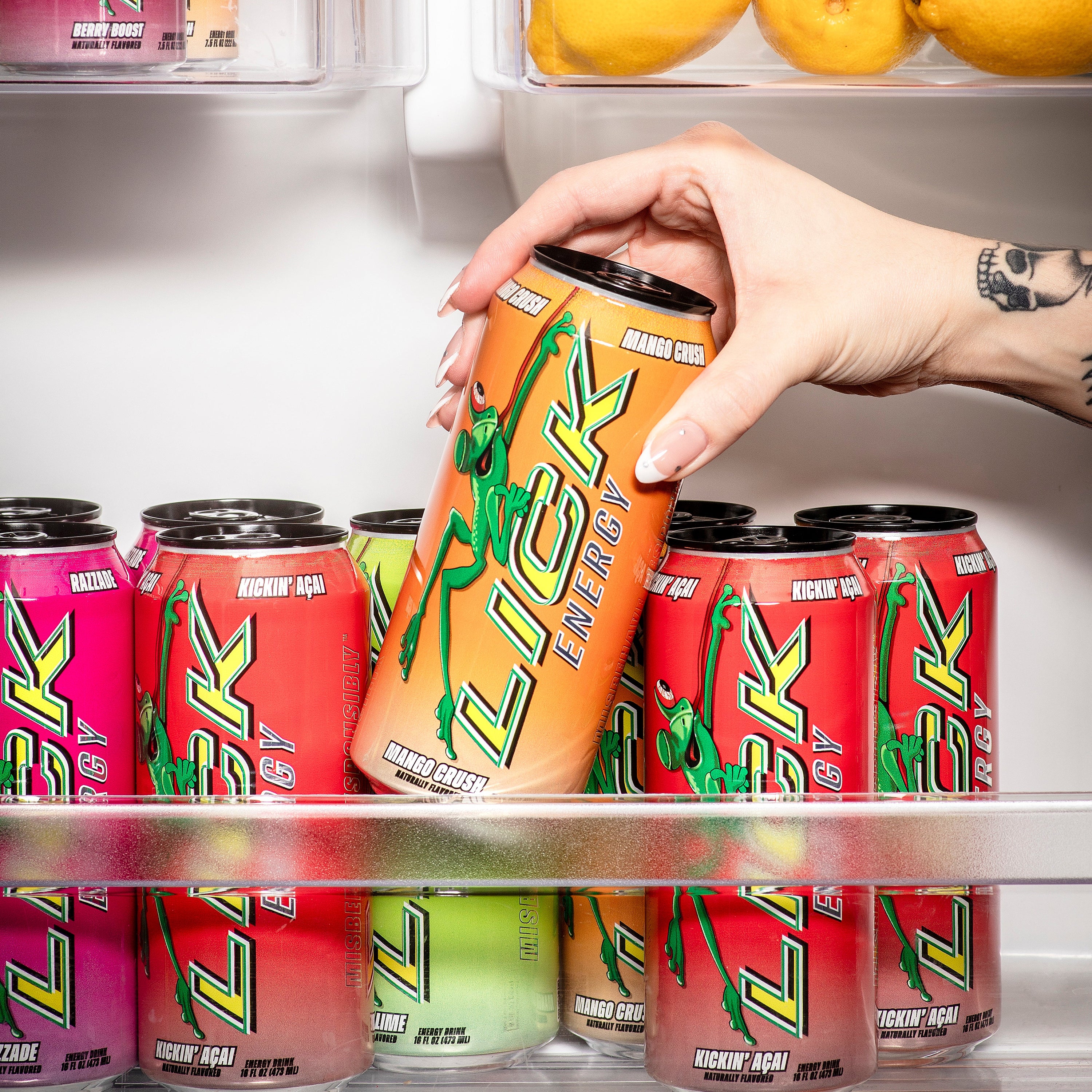 Hand reaching for a can of Lick Energy in a refrigerator with other colorful cans and lemons.