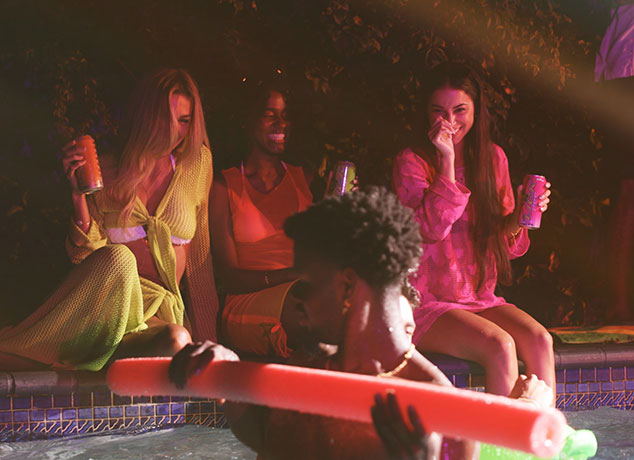 Group of people by a pool at night, enjoying Lick Energy drinks and time together.